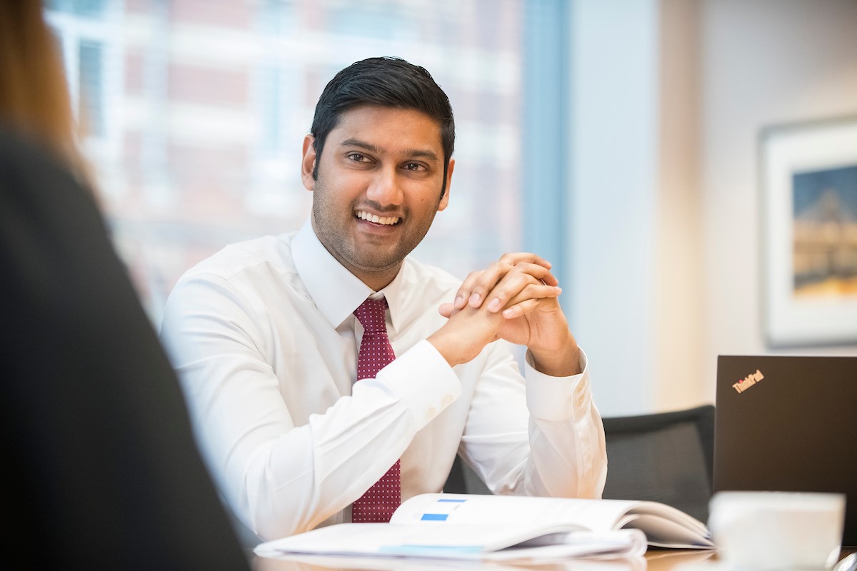 Smiling man in white shirt with hands clasped at desk