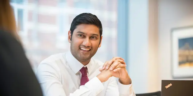 Smiling man in white shirt with hands clasped at desk